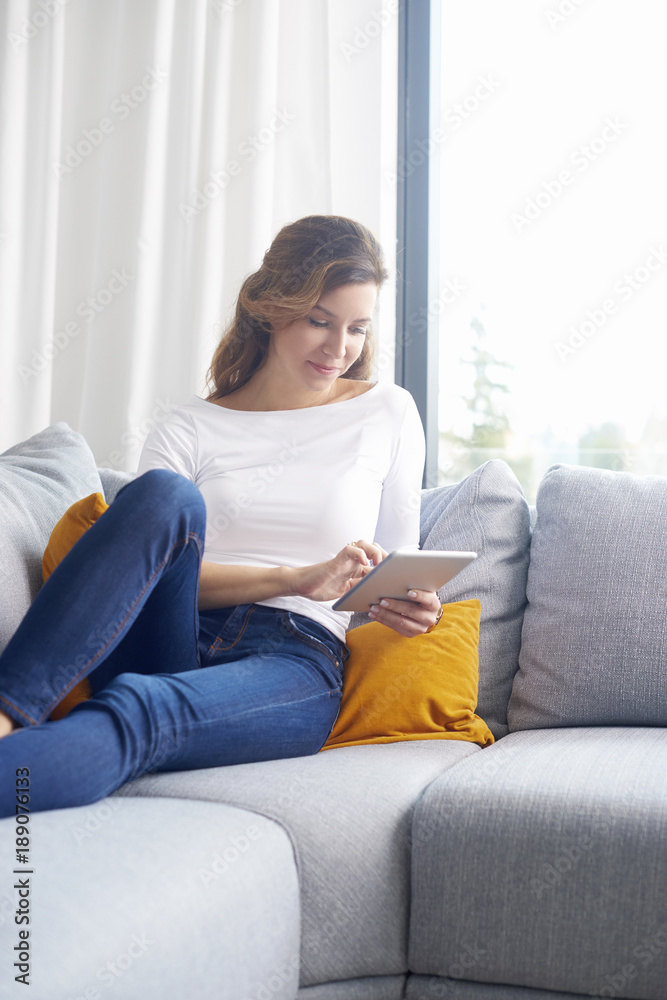 Woman browsing on the internet. Smiling middle aged woman using digital tablet while relaxing on sofa at home. Woman browsing on the internet. Smiling middle aged woman using digital tablet while relaxing on sofa at home.
