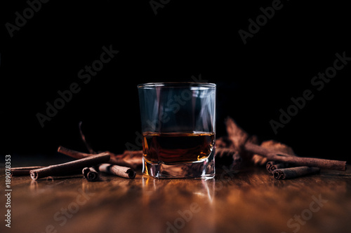 Close-up of a glass of whisky with cinnamon sticks on a table photo