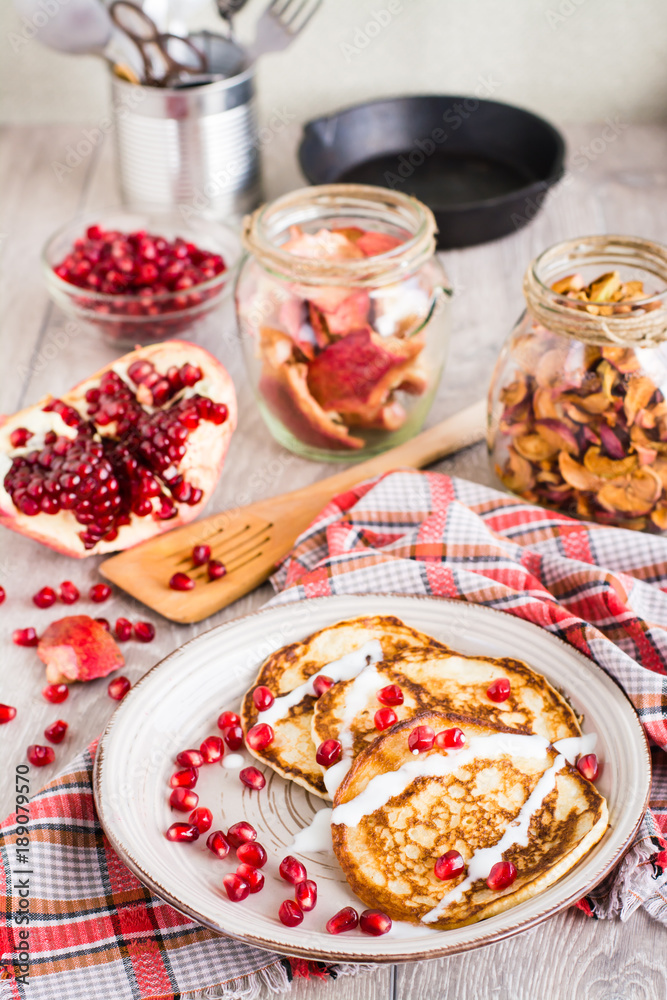 Pancakes with sour cream and pomegranate seeds on a plate.