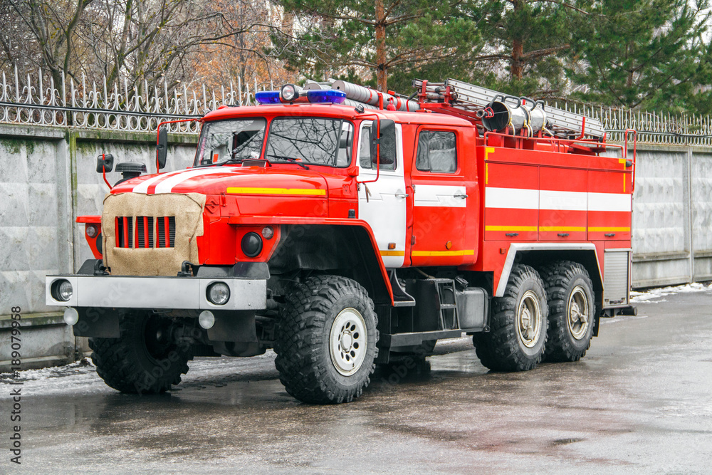 The fire truck in full equipment rushes to a challenge along the asphalt road next to the concrete fence. The fire truck in full equipment rushes to a challenge along the asphalt road next to the concrete fence.