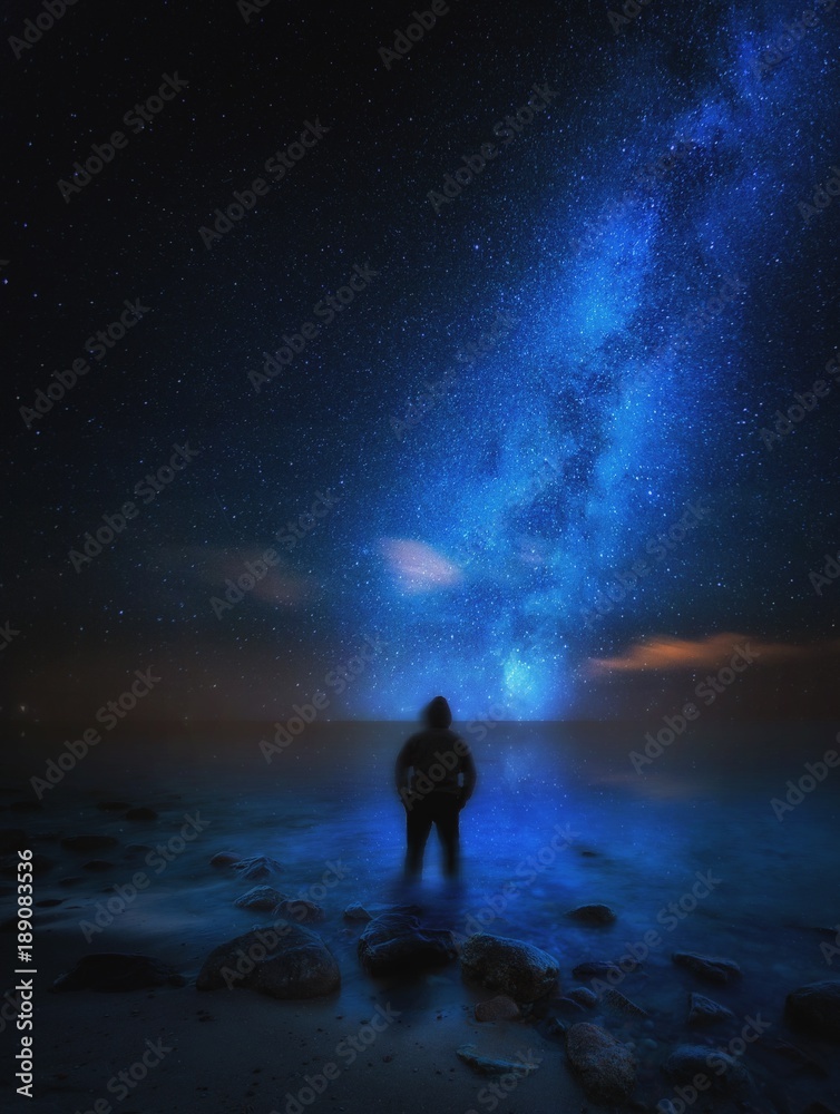 Strange man (silhouette) standing on sea shore and watching milky way