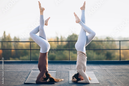 Two young women doing double yoga asana supported headstand on the roof outdoors photo