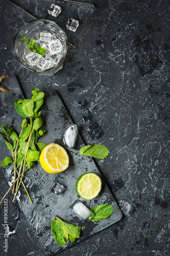 Mojito cocktail making. Mint, lime, glass, ice, ingredients and shaker on black stone background