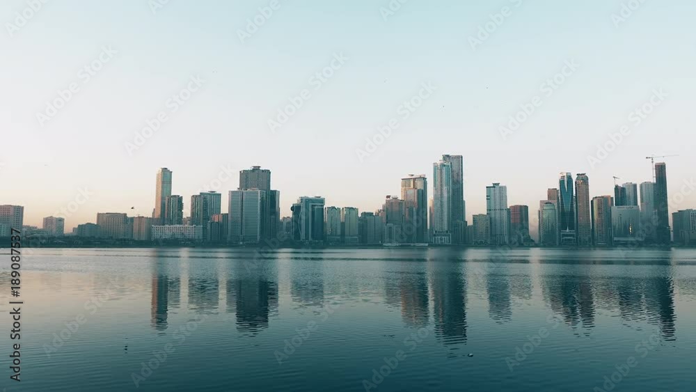 Panning along coast of Khalid lake. Skyline with skyscrapers. Al Noor island in Sharjah, UAE. Blue sky.