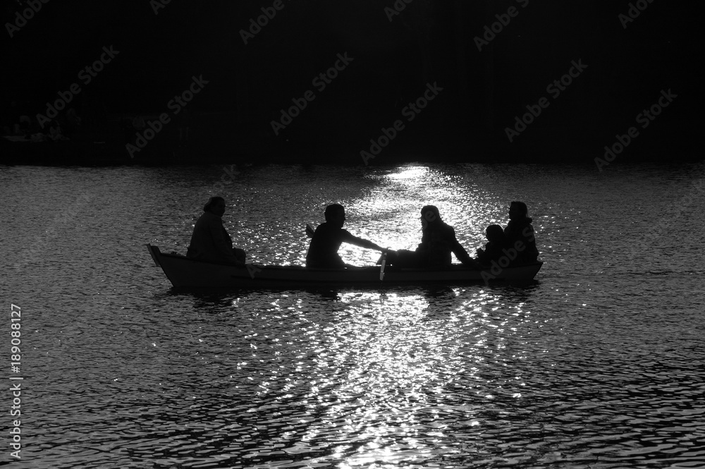 Family in the boat at Daumesnil lake (Paris, France) in sunset glow. Silhouettes. Harmony with nature idea.  Black and white photo.