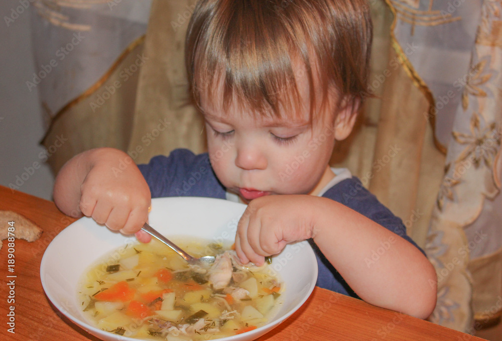 the child is a soup from a plate. A little boy eats his own soup. Child and a bowl of soup. the child is a soup from a plate. A little boy eats his own soup. Child and a bowl of soup.