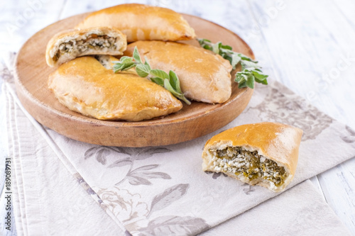 Fresh homemade pies with cheese and greens for breakfast. Portion pies. On a wooden plate and on a white background. Free space for text or advertising.