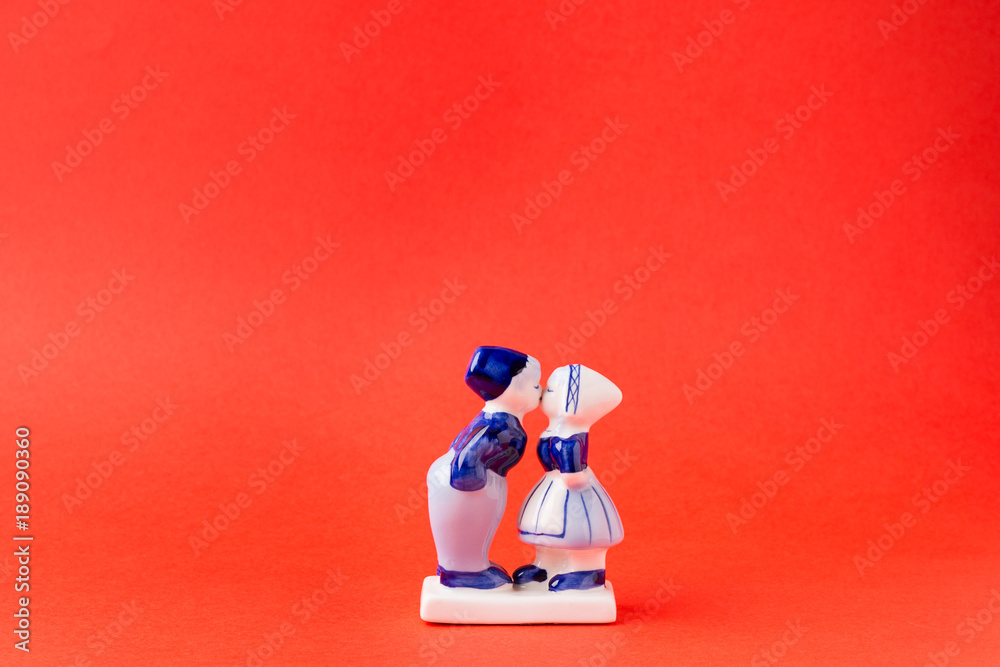 Porcelain figurines of kissing boy and girl in national Dutch costumes on red background. Saint Valentine's Day Concept.
