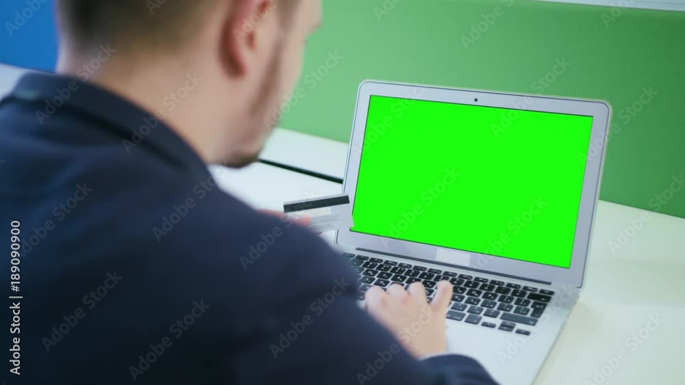 A young man using a laptop with a green screen indoors. Close-up shot. Soft focus. A young man using a laptop with a green screen indoors. Close-up shot. Soft focus.