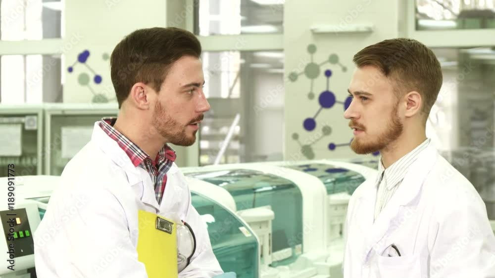 Two young lab technicians stand in the middle of the laboratory and talk Two young lab technicians stand in the middle of the laboratory and talk