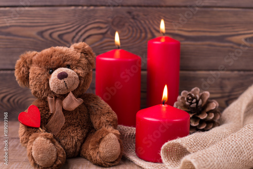 Valentine's day concept. Teddy bear keeps the heart, candles and a bump on wooden background. Selective focus.