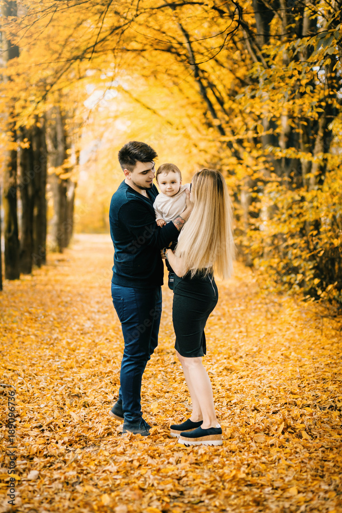 young family and newborn son posing for the camera in autumn park young family and newborn son posing for the camera in autumn park