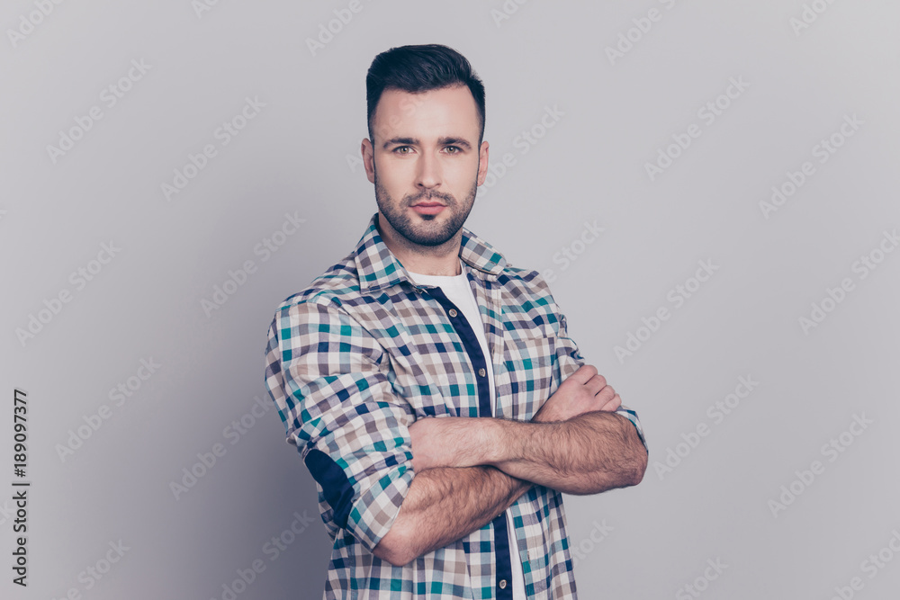 Portrait of young attractive stunning man having his hands crossed, looking at camera with serious expression, standing over grey background Portrait of young attractive stunning man having his hands crossed, looking at camera with serious expression, standing over grey background