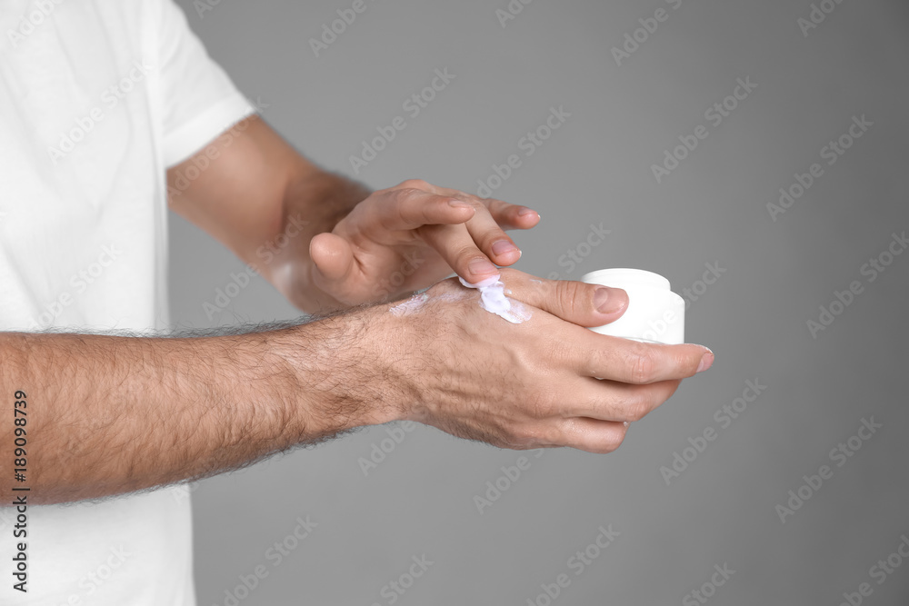 Man applying hand cream on grey background Man applying hand cream on grey background