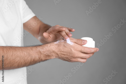 Man applying hand cream on grey background