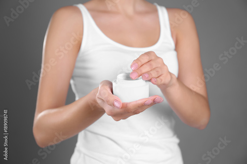 Young woman with jar of hand cream on grey background