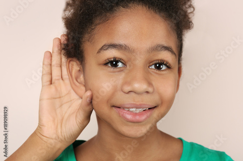 Little African-American girl with hearing problem on light background