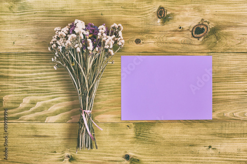 Beautiful bouquet of flowers and empty paper for text on wooden table.