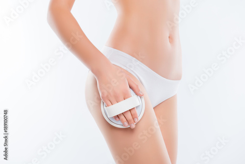 Cropped close up photo of sexy thin slim pure clean clear skinny woman's hips and legs wearing white classic underlinin underclothes, she is using brush for massaging body isolated on background
