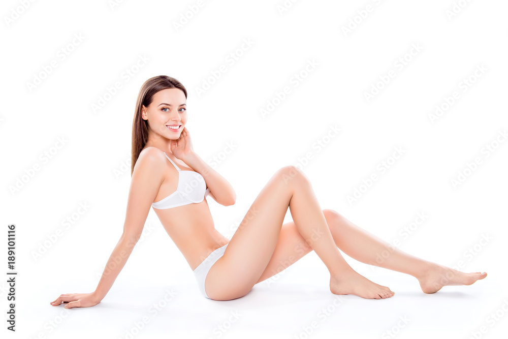 Slender, attractive, slim, charming, pretty woman sitting over white background in bra and bikini, looking at camera, demonstrating her perfect body, plain skin, wellness, wellbeing concept