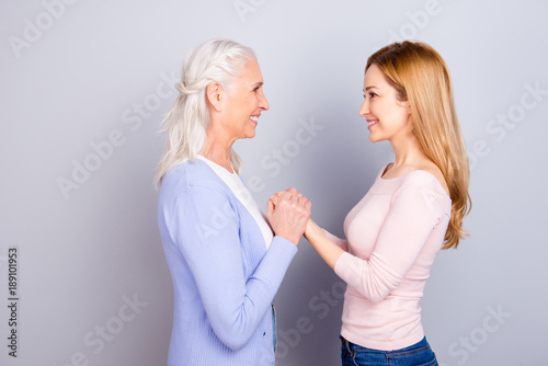 Two charming adorable wonderful dreamy darling dear beautiful cheerful excited joyful mama and kind friendly attentive sensitive daughter holding hands looking at each other isolated gray background