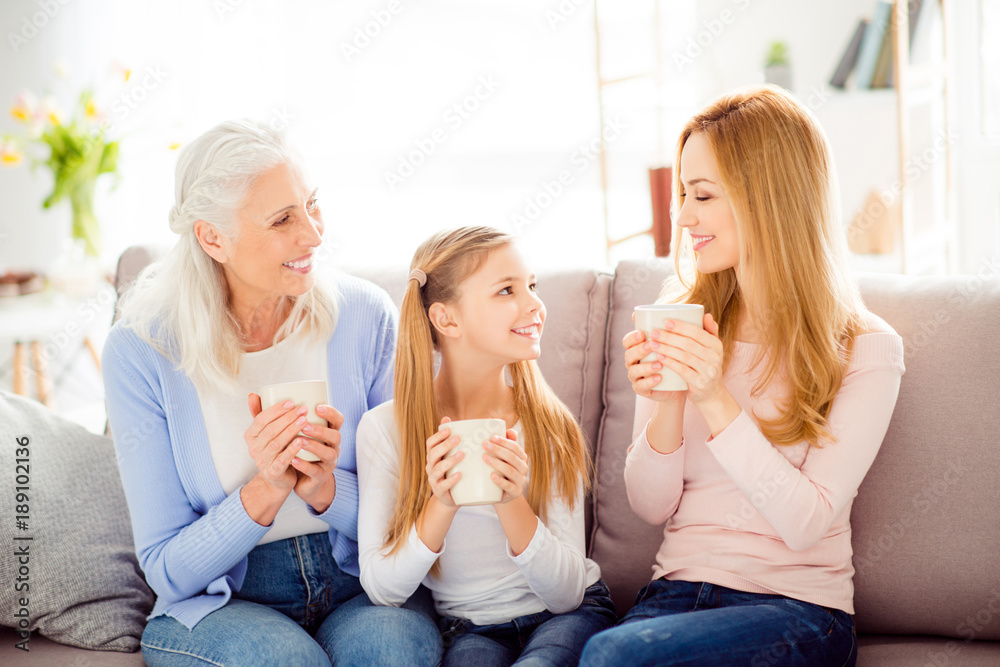 Grandparents comfort friendship relationship people generation leisure concept. Beautiful pretty cheerful mum telling gossiping with curious schoolgirl and granny on divan holding cups