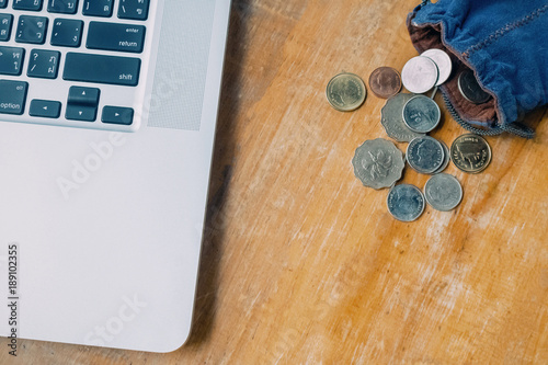 Laptop and many Money coins in the blue bag on wood table photo