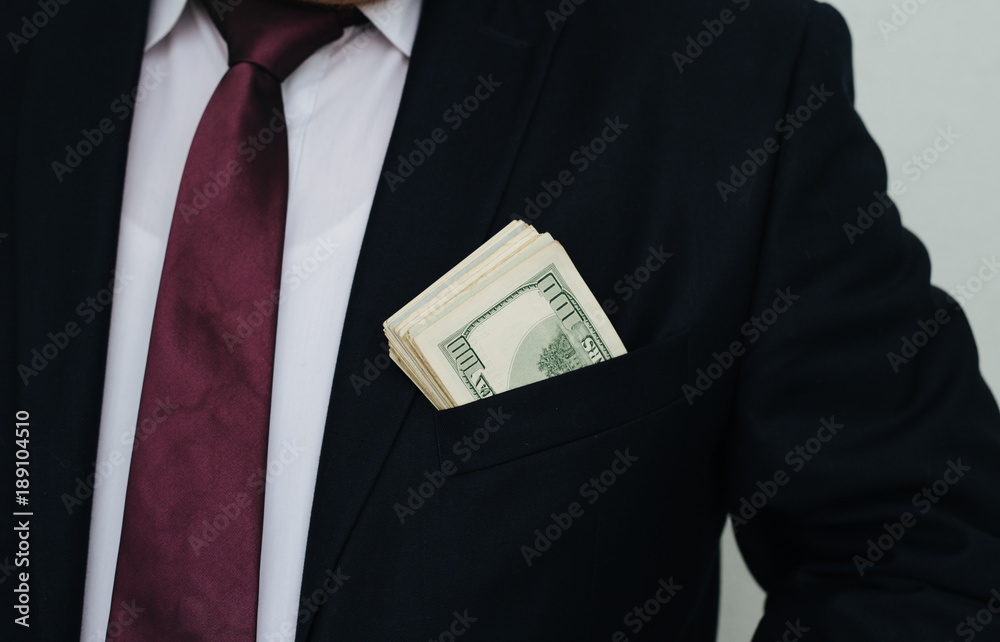 A businessman shows a sum of cash, puts it in his pocket of suit