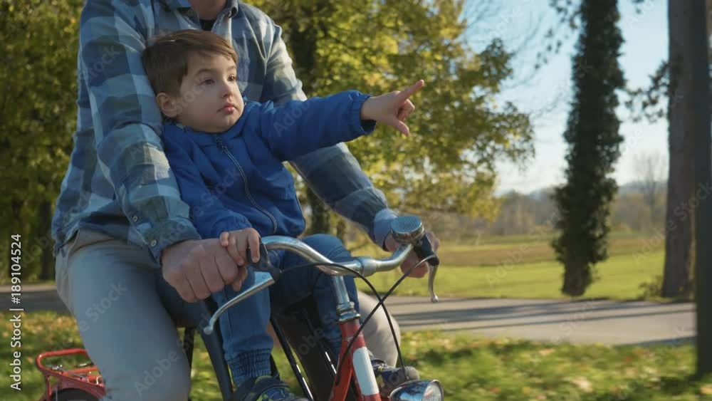 Tracking shot - Adorable boy on a front child seat smiling enjoying bicycle ride with his dad on a sunny day in the city park.
Tracking shot - Adorable boy on a front child seat smiling enjoying bicycle ride with his dad on a sunny day in the city park.