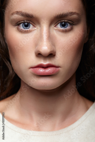 Beauty portrait of young woman. Brunette girl with bright blue eyes and day female makeup on gray background