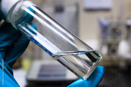 Chemical transparent liquid in clear bottle holding by chemistry hand in green chemical resistance glove.