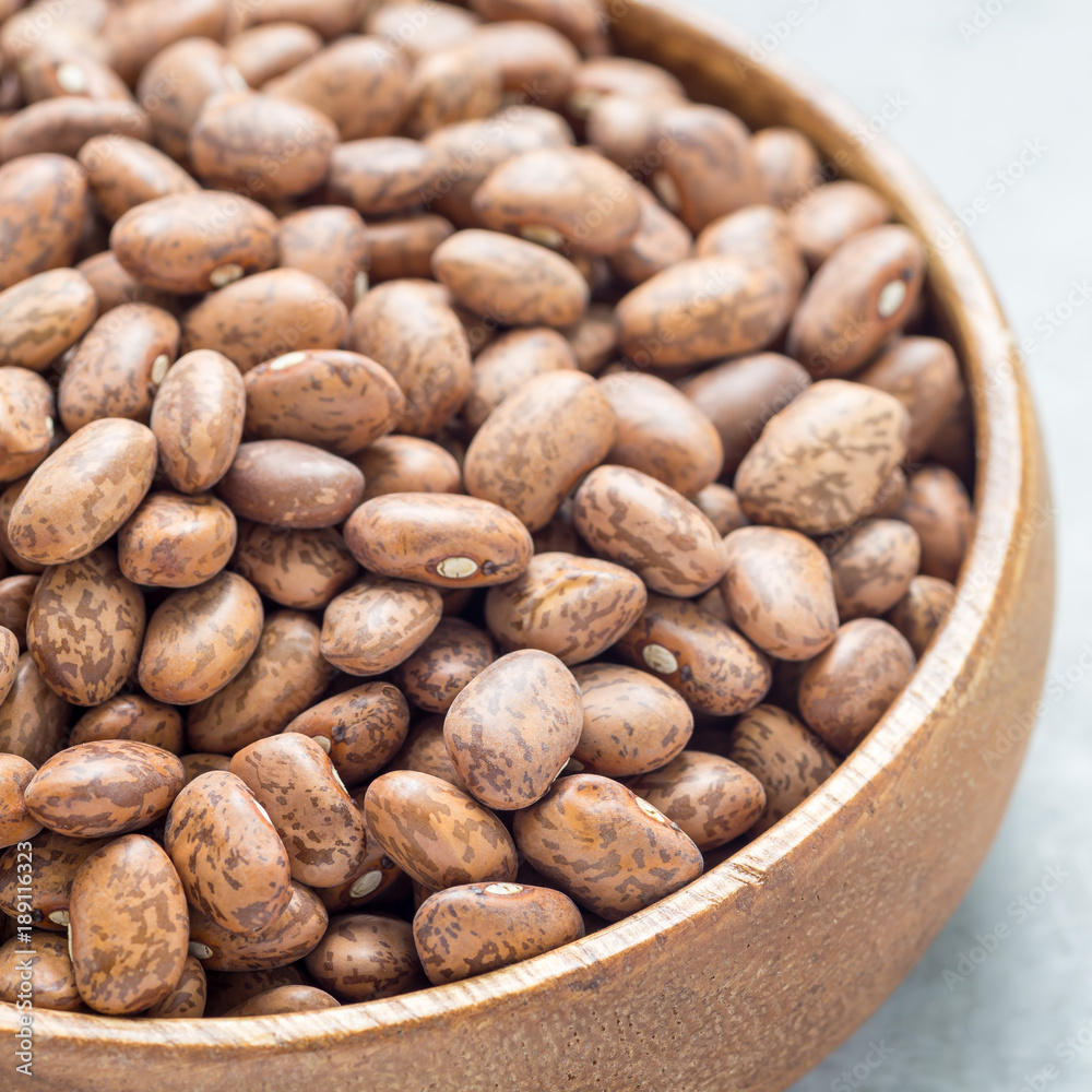 Uncooked dry pinto beans in a wooden bowl, square format Uncooked dry pinto beans in a wooden bowl, square format