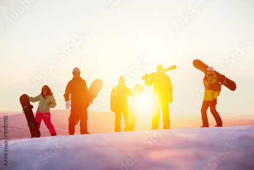 Group of serious friends with ski and snowboards against sunset