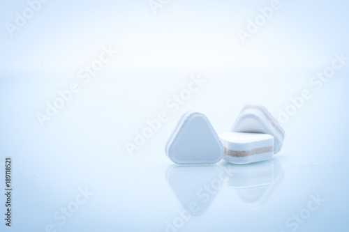 Macro shot of triangle shape tablet pills. Three layers tablet pills for indication antacid, digestive and gastric pain. Group of sandwich tablets pills on white background with copy space for text. photo