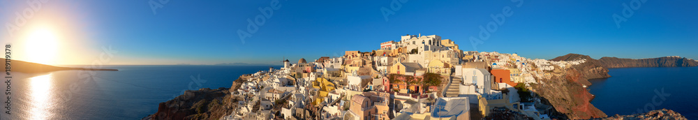 Sunset over Santorini island in Greece. Traditional church, apartments and windmills in Oia village.
