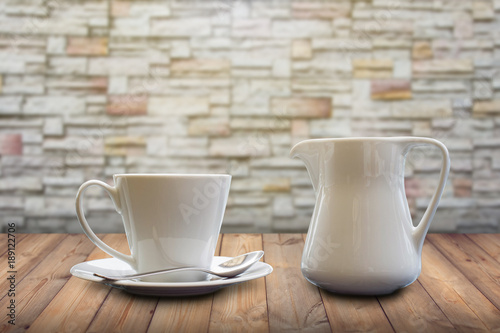 A cup of coffee and milk pot on wooden table and stone background.
