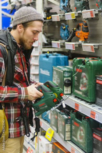 Young man enthusiastically compares electric jig saws at a large store photo