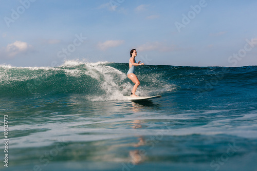 Photography Young woman in bright bikini surfing on a board in ocean