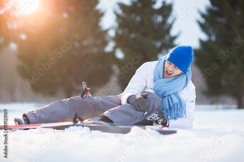 Young skier screaming and keeping his hands on hurt knee while lying in snowdrift