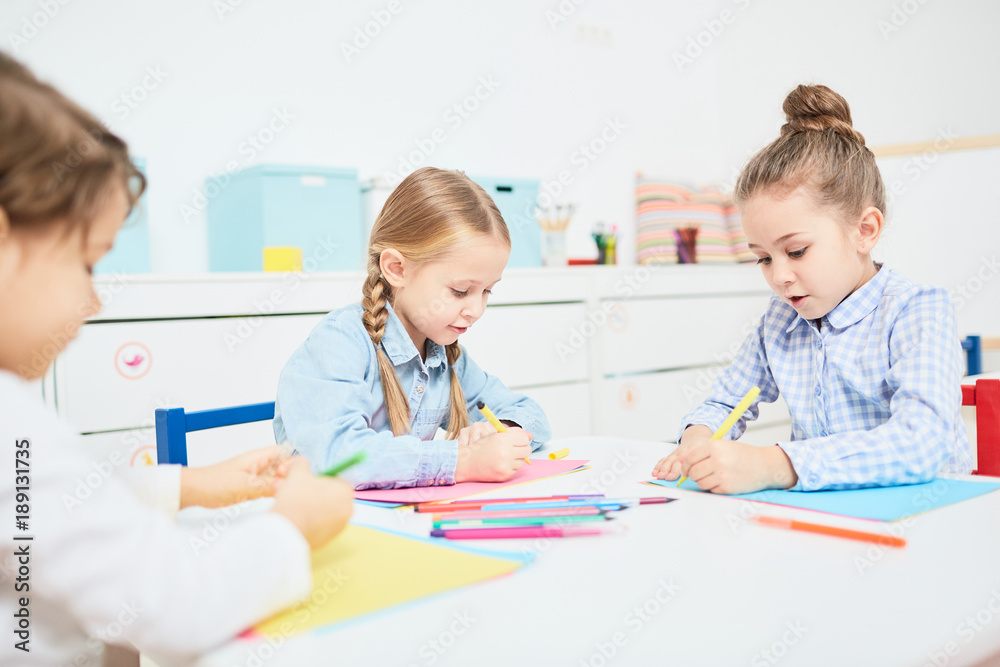 Group of little kids, two girls and boy, drawing with crayons in kindergarten Group of little kids, two girls and boy, drawing with crayons in kindergarten