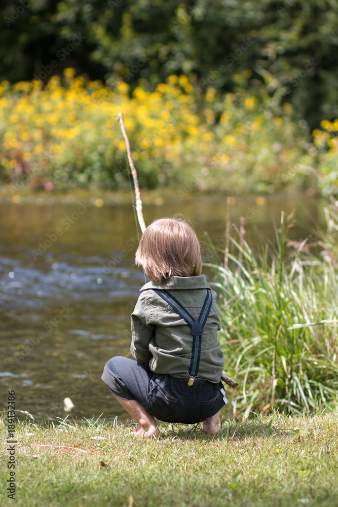 Little boy sitting on a river shore with old-fashioned fishing rod Stock  Photo
