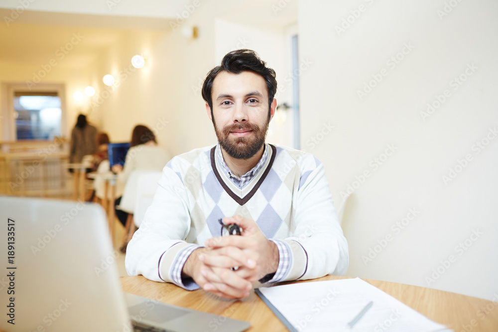 Elegant businessman sitting by table with laptop in front and looking at camera Elegant businessman sitting by table with laptop in front and looking at camera