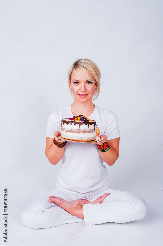 Fototapeta premium Yogi girl in a white suit holding a cake and wants to bite him. The concept of a healthy lifestyle, healthy sweets