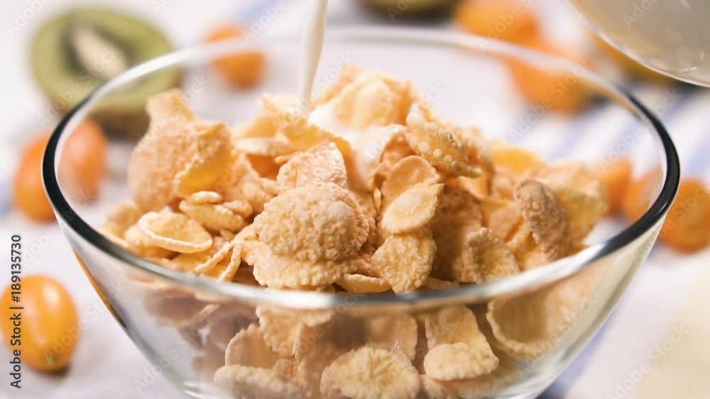 Pouring milk into a bowl of cornflakes, slow motion. Healthy breakfast of cornflakes with milk, close up. Pouring milk into a bowl of cornflakes, slow motion. Healthy breakfast of cornflakes with milk, close up.