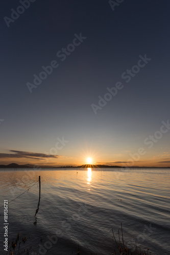 Beautiful sunset over Trasimeno lake (Umbria), with sun coming down behind an island and some fishing nets in the foreground