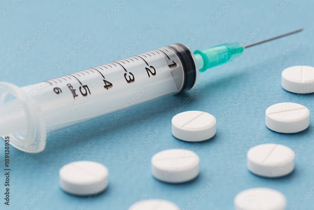 White pills and syringe on a blue background White pills and syringe on a blue background