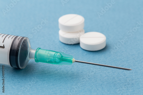 White pills and syringe on a blue background