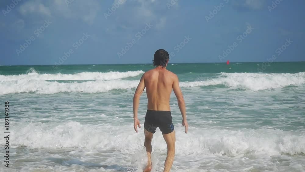 Handsome young man runs into the sea in slow motion. happy summer vacation swims relax recreation on waves. 1920x1080