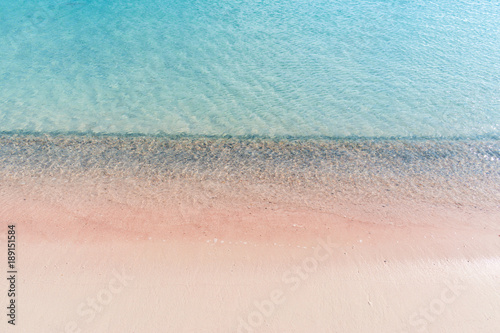 Soft waves of the sea on the pink sand and beautiful beach with cliffs.Coast of Crete island in Greece. Pink sand beach of famous Elafonisi