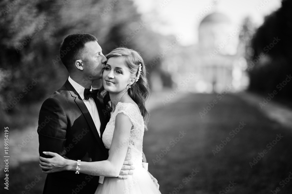 Lovely wedding couple walking along the green alley which leads to a church. Black and white photo. Lovely wedding couple walking along the green alley which leads to a church. Black and white photo.